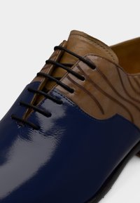 Μπλε παπούτσι από δερμάτινο βινύλιο με καφέ δερμάτινο επάνω μέρος, με υφή σχεδίου, μαύρα κορδόνια και κομψό μυτερό σχήμα μύτης.