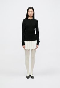 Top negru cu mâneci lungi, cu dungi, asortat cu o fustă plisată crem, ciorapi opaci albi și pantofi negri cu vârf închis. Design simplu, minimalist.