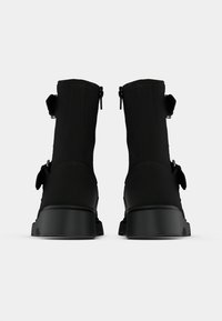 Μαύρα μποτάκια αστραγάλου με λεία υφή, που διαθέτουν πλαϊνά φερμουάρ και διπλές λουρίδες ως αξιοσημείωτες λεπτομέρειες. Χοντρά μαύρα подошвы προσφέρουν σταθερότητα.