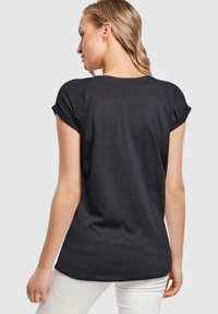 Sort T-shirt med korte ærmer, rund halsudskæring, blødt stof, opkrøllede ærmekanter og en let buet nederste kant.