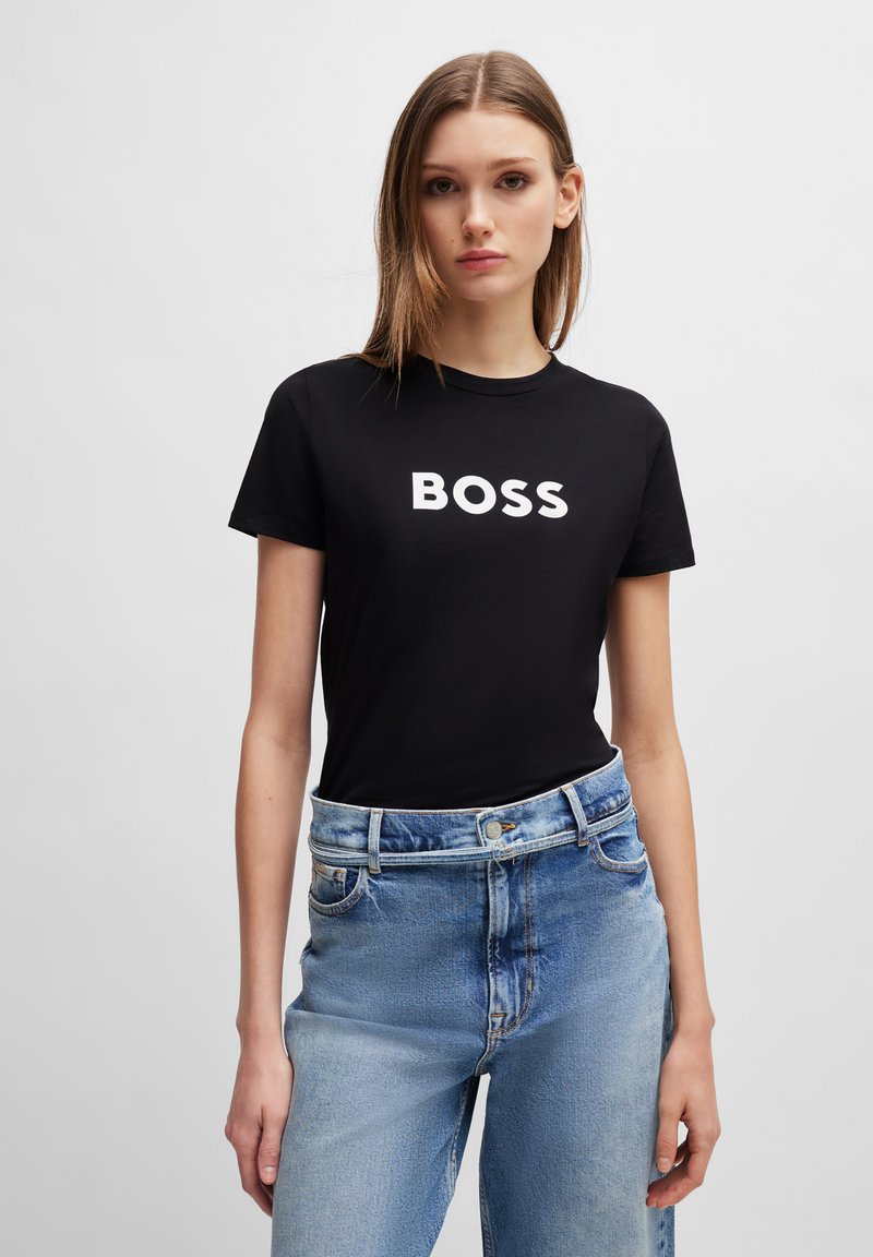 T-shirt noir en coton avec le grand texte blanc "BOSS" sur le devant, associé à un jean taille haute bleu clair. Design et coupe simples.