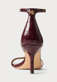 Μπορντό δερμάτινο ψηλοτάκουνο παπούτσι με σχέδιο κροκοδείλου, λουρί στον αστράγαλο και χρυσό λογότυπο στη ζώνη. Ανοιχτή μύτη με λεπτό στιλέτο τακούνι.