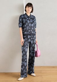 Πλεκτή μαύρη ενδυμασία με μπλε ουράνια σχέδια; περιλαμβάνει ένα κοντομάνικο πόλο και παντελόνι με φαρδιά πόδια. Έχει αξεσουάρ μια ροζ τσάντα και μπεζ παπούτσια.