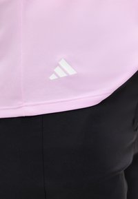 Κοντινό ενός ρόζ ρούχου με λευκό λογότυπο Adidas πάνω από μαύρο παντελόνι.