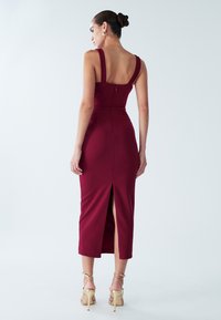 Bordo midi suknelė su plačiomis petnešėlėmis, aptempta siluetu ir užtrauktuku gale. Suknelėje yra aukštas plyšys prie šlaunies, suteikiantis papildomo detalių.