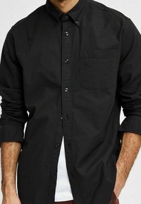 Camicia nera con bottoni in tessuto di cotone, dotata di taschino sul petto, maniche lunghe e colletto con finitura liscia e bottoni a contrasto.