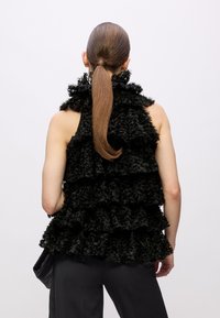 Zwarte ruches mouwloze top met gelaagd ontwerp. Beschikt over een gestructureerde oppervlakte, hoge halslijn en een losse fit. Gecombineerd met donkere broek.