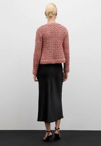 Gehaakte roze cardigan met open weving, lange mouwen en een cropped fit, gecombineerd met een zwarte satijnen midi-rok en zwarte sandaaltjes met banden.