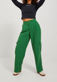 Groene wijde cargobroek van gladde stof, met meerdere zakken, een hoge taille en een relaxte pasvorm. Gecombineerd met een zwart cropped top.