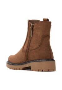 Botín de ante marrón con cremallera lateral, suela de goma gruesa y detalles de costura sutiles. Diseñado para la practicidad y la comodidad.