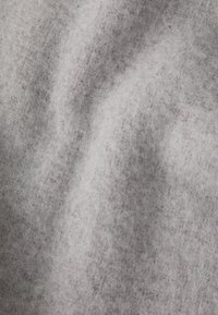 Tissu en laine gris avec une texture douce et pelucheuse, présentant des variations subtiles de ton, des plis et un léger éclat.