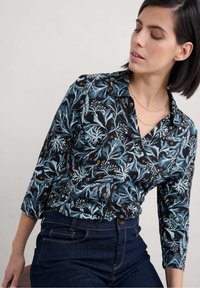 Blusa nera a fiori con maniche a tre quarti, caratterizzata da motivi verde bluastro e oro, colletto classico e una linea aderente.