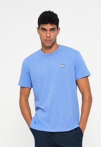 Világoskék pamut póló, kerek nyakkivágással, rövid ujjakkal és egy kis logóval a mellkason. Sima tapintású, laza illeszkedés.