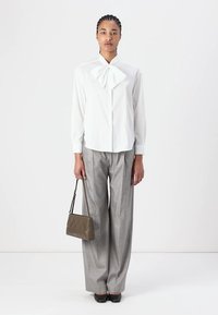 Camicia bianca con dettaglio a fiocco, pantaloni a gamba larga grigi a quadri, scarpe nere e una piccola borsa verde oliva con design a zigzag.