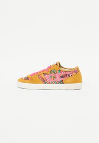 Baskets en daim avec un dessus jaune, des lacets roses et un milieu en textile à motifs multicolores, avec une semelle en caoutchouc blanc.