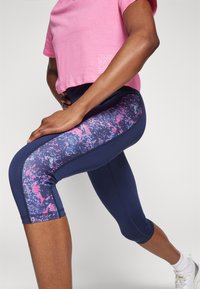 Navy capri leggings with a colorful, abstract pattern on the sides. Paired with a light pink, short-sleeve workout top.