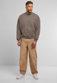 Brązowa bluza z napisem "Problemy psychiczne", w połączeniu z luźnymi beżowymi spodniami i białymi sneakersami. Casualowy, wygodny design z prążkowanymi mankietami.