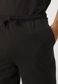 Fekete pamut joggerek elasztikus derékkal, állítható zsinórral és oldalsó zsebekkel. Simaság jellemzi, testhez simuló fazonnal, enyhe rugalmassággal.