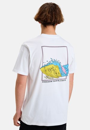 Camiseta blanca de algodón con un gráfico de olas colorido en la parte posterior. El texto debajo dice "LIBERTAD DEL CAOS". Mangas cortas y corte relajado.