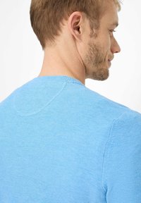 Lyseblå strikket sweater med rund halsudskæring, tekstureret stof og synlige stingmønstre på ryggen og skuldrene.