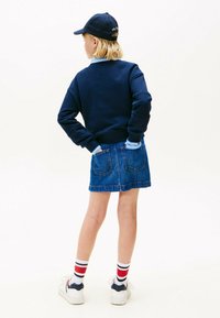 Sudadera azul marino con cuello redondo, falda de mezclilla con bolsillos traseros, zapatillas blancas y calcetines a rayas rojas. Gorra de béisbol con logo.