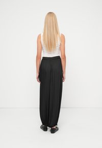 Black pleated wide-leg trousers with a fitted waistband, paired with a fitted white top; a smooth, lightweight fabric and tapered hem.