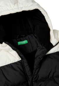 Zateplená bunda s černým vnějším povrchem, smetanovou kapucí, fleece podšívkou a zelenou etiketou uvnitř. Zapínání na zip v přední části.