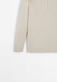 Jasnobeżowa bluzka z długim rękawem wykonana z teksturowanej dzianiny, z półzamkiem przy szyi, prostym dołem i dopasowanymi mankietami.