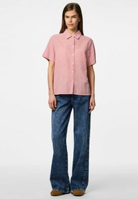 Camicia a righe rossa e bianca con maniche corte e colletto puntato, abbinata a jeans in denim blu svasati. Tessuto morbido, con bottoni davanti.