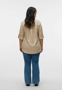 Beige blouse met lange mouwen en opgerolde mouwen, met een losse pasvorm. Gepaard met blauwe flared jeans en zwarte enkellaarsjes.