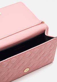 Pink quilted leather handbag with a smooth finish, gold hardware, and a black interior featuring the embossed brand name.