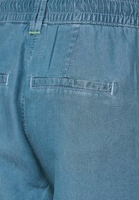 Pantalones de tela chambray azul con cintura elástica, con dos bolsillos traseros con detalles de costura. Textura suave y aspecto ligeramente desgastado.