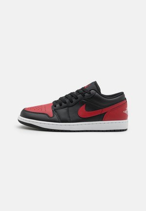 Niedriger schwarzer und roter Nike Sneaker mit rotem Swoosh-Logo und weißer Sohle, von der Seite auf weißem Hintergrund gezeigt.