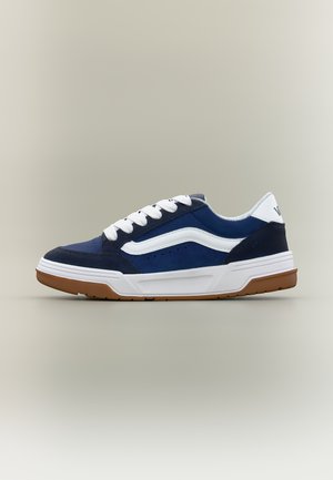 Baskets basses bleu marine et blanches avec des lacets blancs et une semelle en gomme, vues de côté sur un fond neutre.