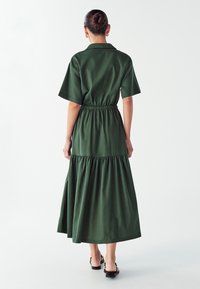Zielona bawełniana sukienka midi z dopasowanym pasem i falbanowym dołem. Krótkie rękawy i kołnierzyk. Gładka faktura.