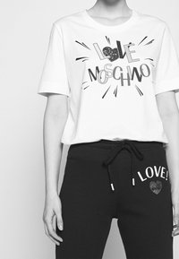 White short-sleeve t-shirt featuring a graphic design with "LOVE MOSCHINO" in black, and black sweatpants with "LOVE!" and a heart accent.