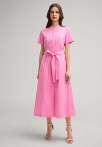 Rosa Baumwollkleid mit hohem Kragen, kurzen Ärmeln, gefälteten Details und gebundenem Taillenteil. Die Länge reicht bis zur Mitte der Waden; glatte Textur, simples Design.