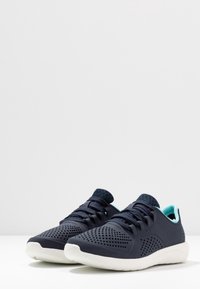 Chaussures de sport légères en bleu marine et aqua, dotées d'une tige respirante perforée, de lacets texturés et d'une semelle blanche amortie.