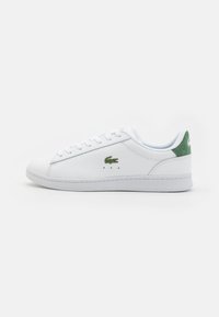 Sneaker bianco in pelle con un accento in suede verde sul tallone. Presenta un design con lacci, un piccolo logo verde e dettagli perforati sui lati.