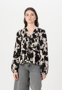 Bluza s dugim rukavima, apstraktnog uzorka u crnoj i krem boji, s v-izrezom i detaljem u naborima u struku. Izrađena od laganog materijala.