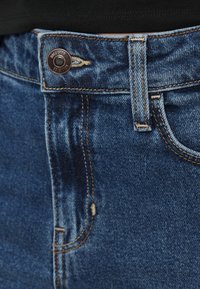 Τζιν παντελόνι σε σκούρο μπλε χρώμα με λεία υφή, διαθέτει ραφές σε αντίθεση, κλείσιμο με μεταλλικό κουμπί και κλασικό σχέδιο με πέντε τσέπες.