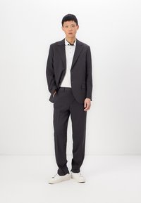 Donkergrijze maatpak met een enkelvoudige blazer, bijpassende broek en een witte poloshirt, aangevuld met witte sneakers.