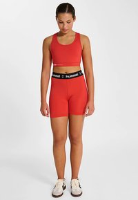 Roter Sport-BH und passende Shorts aus dehnbarem Stoff, mit einem schwarzen Bund und "hummel"-Logo. Glatte Textur und figurbetontes Design.