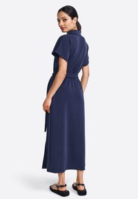 Abito blu navy con colletto, maniche corte e vita con cintura. Il tessuto sembra morbido, con un design lungo fino al ginocchio e spacchi laterali.