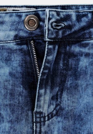 Jean en denim dans un délavage bleu moyen, avec une fermeture éclair, un bouton en cuivre et des détails cousus autour des poches et de la taille.