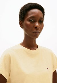 T-shirt a maniche corte di colore giallo chiaro con scollatura rotonda e maniche arrotolate, caratterizzato da un piccolo logo sul lato sinistro del petto. Tessuto morbido.