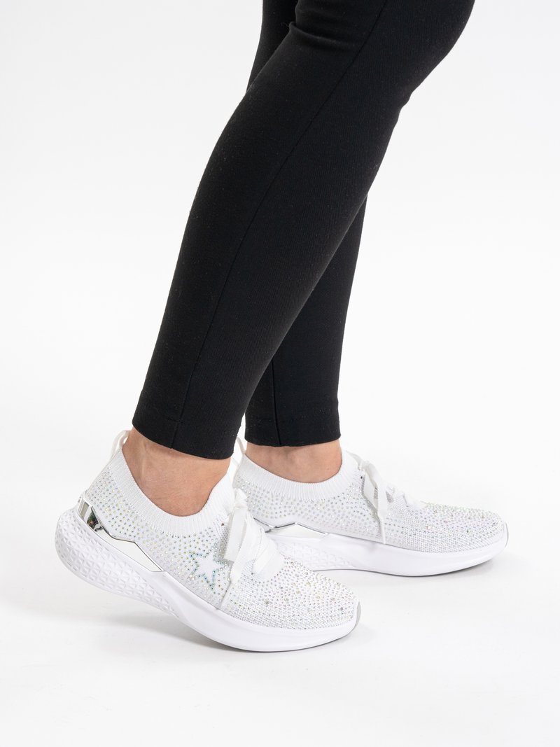 Persona che indossa sneaker bianche in maglia con dettaglio a stella e strass, abbinate a leggings neri su sfondo bianco.