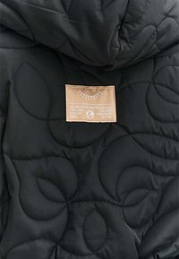 Čierna prešívaná látka s motívmi listov a béžová záplata s ilustráciou zatvoreného oka a inšpirujúcim textom.