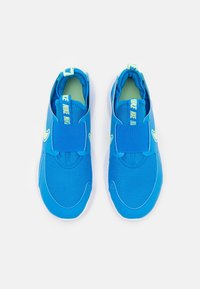Blauwe sportieve schoenen met een gestructureerde mesh bovenkant, elastische band en groene accenten op de binnenzool en de branding. Witte rubberen zool.