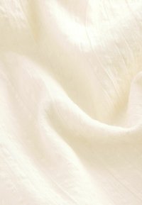 Weißer, strukturierter Stoff mit weichen, fließenden Falten. Das Material wirkt leicht und leicht transparent und zeichnet sich durch eine subtile, natürliche Webart aus.